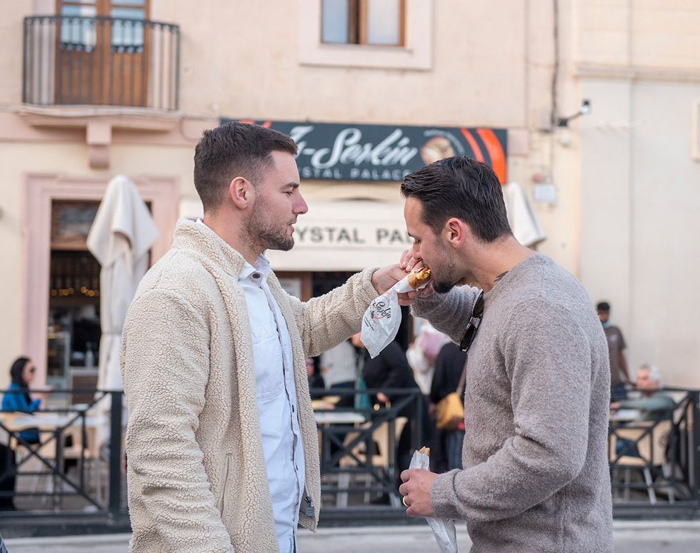 A gay couple enjoying a pastizz, the beloved Maltese snack. Malta unveiled: Your ultimate LGBTQ+ guide to the Mediterranean paradise